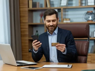 Geschäftsmann sitzt im Büro am Schreibtisch und benutzt Handy und Kreditkarte.