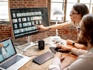 Zwei Angestellte sitzen im Büro am Schreibtisch und ordnen am Computer ihre Bilder in unterschiedliche Ordner.