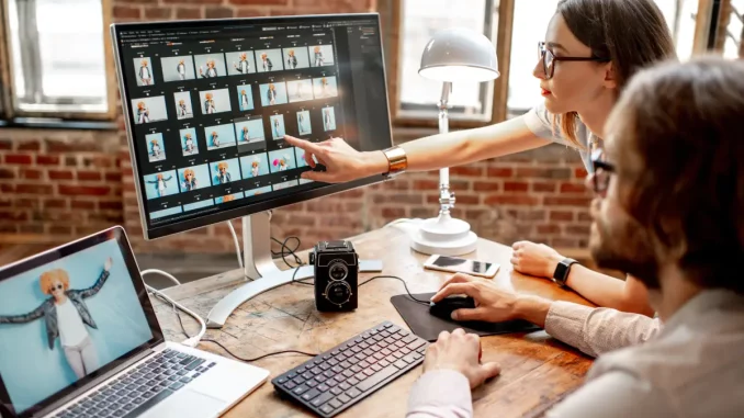 Zwei Angestellte sitzen im Büro am Schreibtisch und ordnen am Computer ihre Bilder in unterschiedliche Ordner.