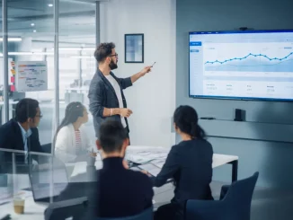 Ein Team von Kollegen hört aufmerksam einer Präsentation mit Beamer-Bilddarstellung zu.