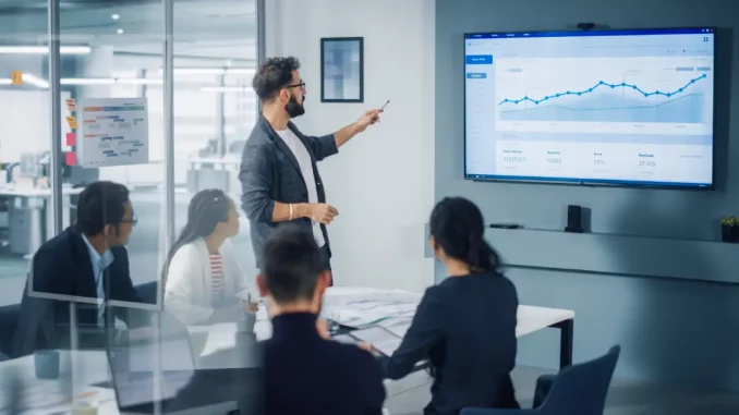 Ein Team von Kollegen hört aufmerksam einer Präsentation mit Beamer-Bilddarstellung zu.