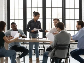 Frau verteilt während eines Meetings im Büro Blätter mit Aufgaben an ihre Kollegen.