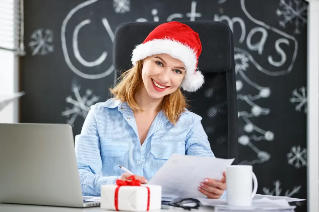 Frau im Businessoutfit sitzt im Büro am Schreibtisch und verfasst ihre handgeschriebenen Weihnachtsgrüße.