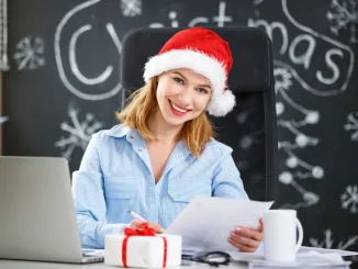 Frau im Businessoutfit sitzt im Büro am Schreibtisch und verfasst ihre handgeschriebenen Weihnachtsgrüße.