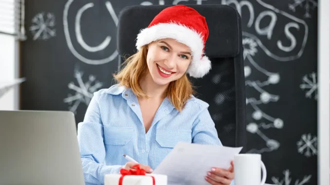 Frau im Businessoutfit sitzt im Büro am Schreibtisch und verfasst ihre handgeschriebenen Weihnachtsgrüße.