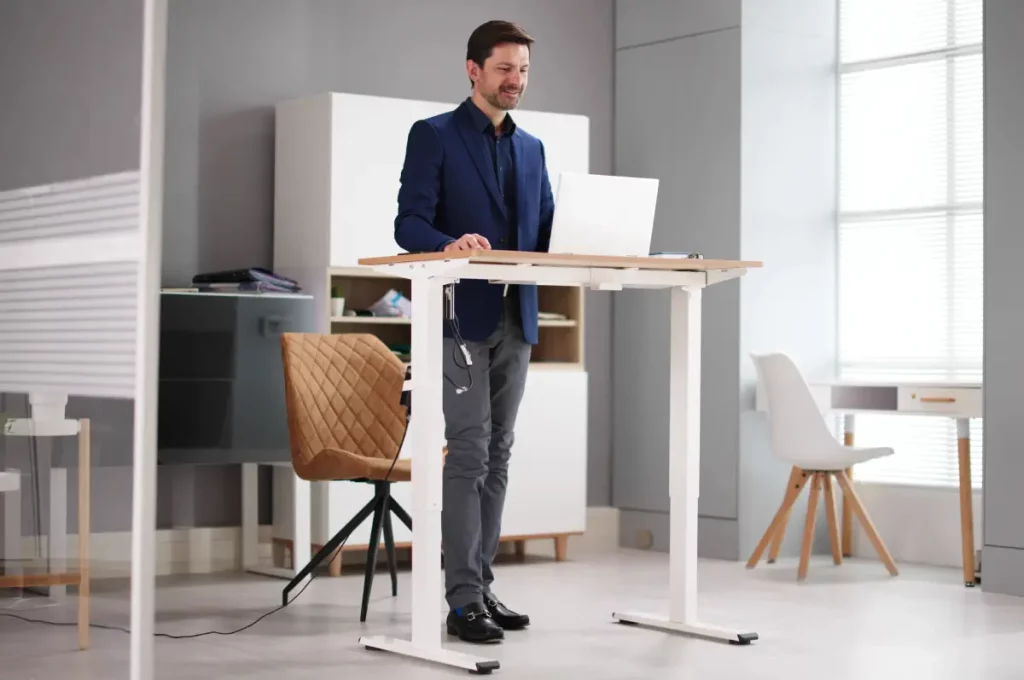 Ein Mann im Business-Outfit steht an einem erhöhten Schreibtisch, auf dem sich ein Laptop befindet.