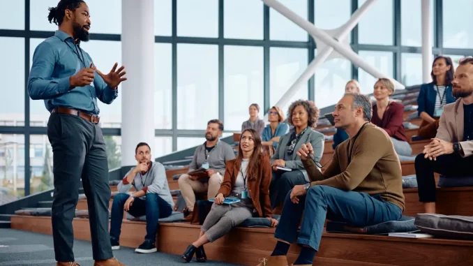 Geschäftsmann spricht zu einer großen Gruppe von Mitarbeitern während einer Bildungsveranstaltung im Konferenzsaal.