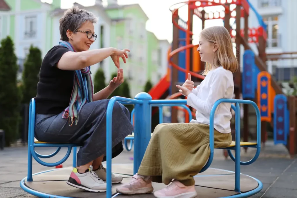 Eine Frau und ein Kind sitzen auf einem Karussel auf dem Spielplatz und kommunizieren über Gebärdensprache.