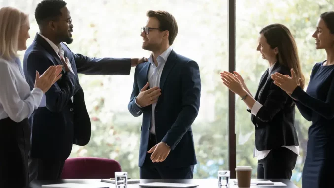 Ein Mann im Business-Outfit bringt einem Kollegen seine Anerkennung und Wertschätzung zum Ausdruck, in dem er ihm motivierend den Arm auf die Schulter legt.
