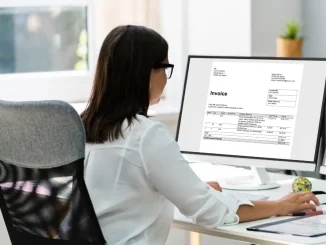 Eine Frau sitzt am Schreibtisch im Büro. Auf ihrem Computer ist ein Rechnungsprogramm geöffnet.