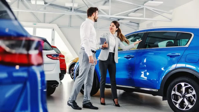 Ein Mann und eine Frau stehen in einem Autohaus vor einem neuen SUV. Es wirkt, als führe die Frau ein Verkaufsgespräch.