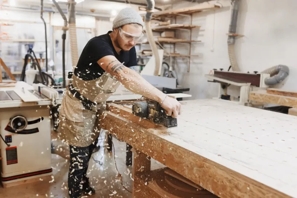 Schreiner bei der Arbeit mit einer elektrischen Hobelmaschine an einem Holzbrett in der Werkstatt.