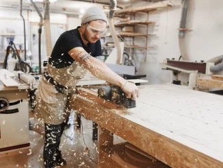 Schreiner bei der Arbeit mit einer elektrischen Hobelmaschine an einem Holzbrett in der Werkstatt.