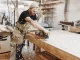 Schreiner bei der Arbeit mit einer elektrischen Hobelmaschine an einem Holzbrett in der Werkstatt.