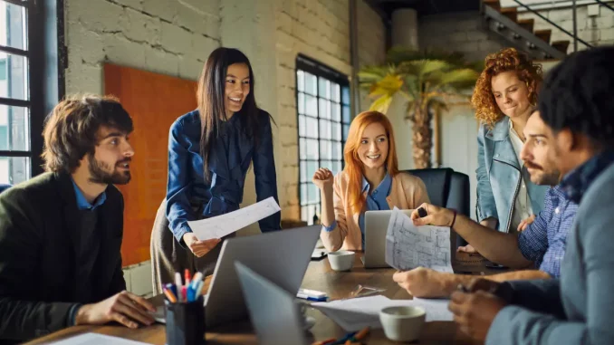 6 Büroangelstellte im Business-Outfit sitzen im modernen Office am großen Meeting-Tisch.