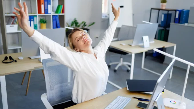 Nahaufnahme einer Frau, die am Schreibtisch sitzt und sich streckt.