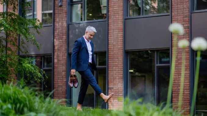 Ein Mann im Business-Anzug läuft barfuß über eine Wiese.