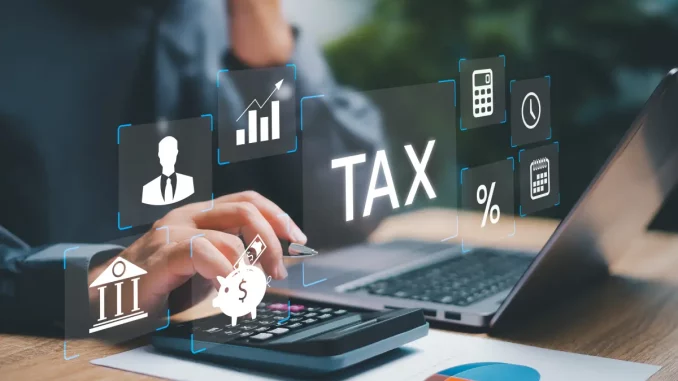 Ein Laptop und ein Taschenrechner liegen auf einem Tisch. Über den elektrischen Geräten ist das Wort Tax sowie das Symbol eines Diagramms und ein Prozentzeichen grafisch dargestellt, um den Bezug zur Betriebsprüfung herzustellen.