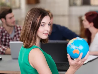 Im Fokus des Bildes ist eine Frau zu sehen, die eine kleine Weltkugel in der Hand hält. Sie sitzt mit Kollegen in einer Besprechung an einem Tisch. Auf dem Tisch stehen Laptops.