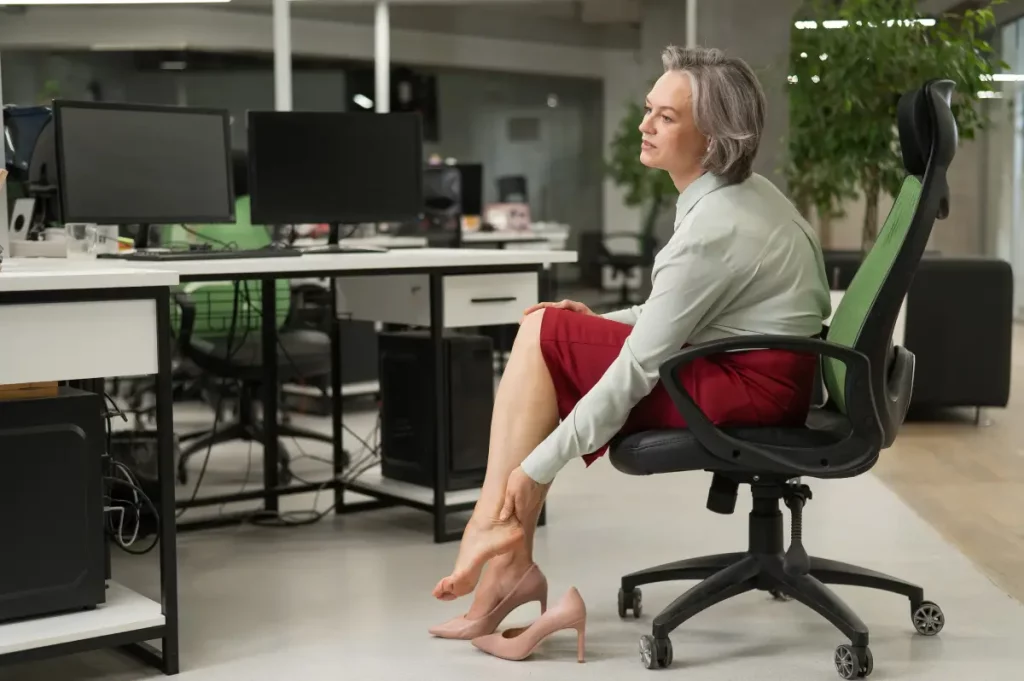 Eine Frau sitzt auf einem Bürostuhl und massiert sich die linke Wade.