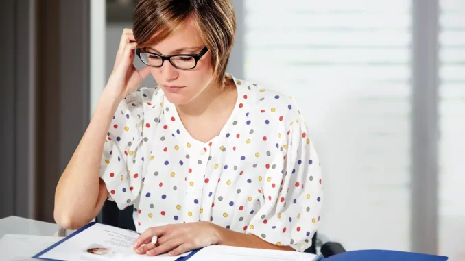 Eine Frau im Business-Outfit sitzt im Büro am Schreibtisch und sieht sich eine Bewerbungsmappe an.