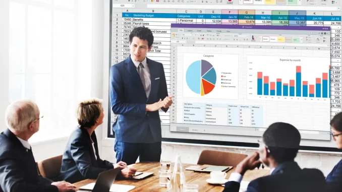 Bild zum Thema "Marketing Mix – Mit der 4-P-Kombination verkaufen": Ein Mann präsentiert vor einem Projektorbild mit Charts, während Kollegen aufmerksam zuhören.