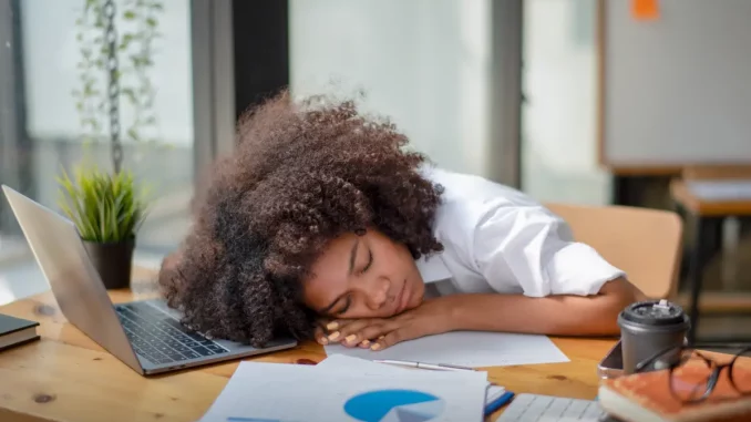 Eine Frau liegt mit dem Kopf auf ihrem Schreibtisch, um ein kurzes Powernapping einzulegen.