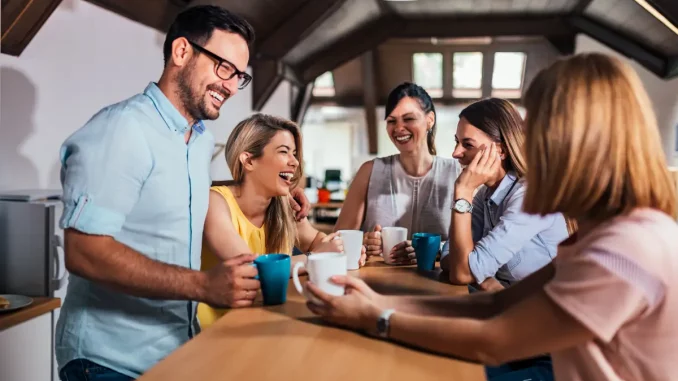 Fünf Kollegen stehen in der Büroküche am Tresen, mit einer Kaffeetasse in der Hand und unterhalten sich angeregt.