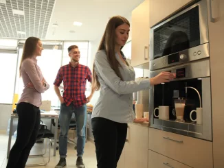 Eine Frau steht in der Unternehmensküche und bereitet sich am Kaffeeautomaten einen Kaffee zu.