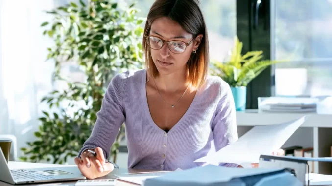 Eine Frau, die freiberuflich arbeitet, schreibt eine Rechnung am Schreibtisch.