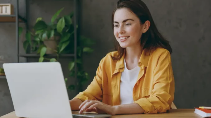 Junge Mitarbeiterin sitzt am Schreibtisch mit Laptop im Büro.