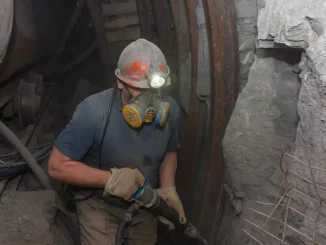 Bergmann mit Atemschutzmaske und Presslufthammer in einem staubigen Kohlebergwerk.