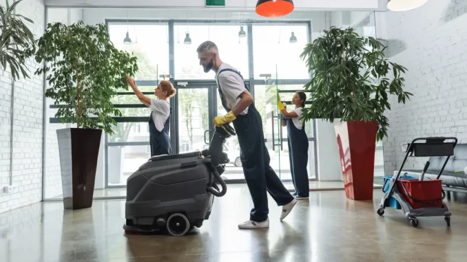 Nahaufnahme von einem Mann in Arbeitskleidung der mit einer Bodenreinigungsmaschine den Eingangsbereich eines Büros reinigt.