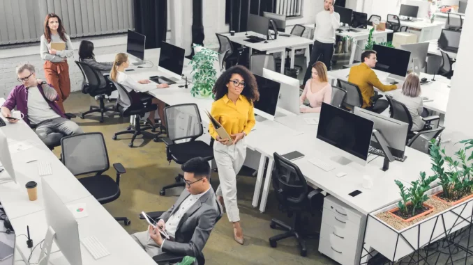 Eine Frau in gelber Bluse sticht im Großraumbüro aus der Menge heraus.