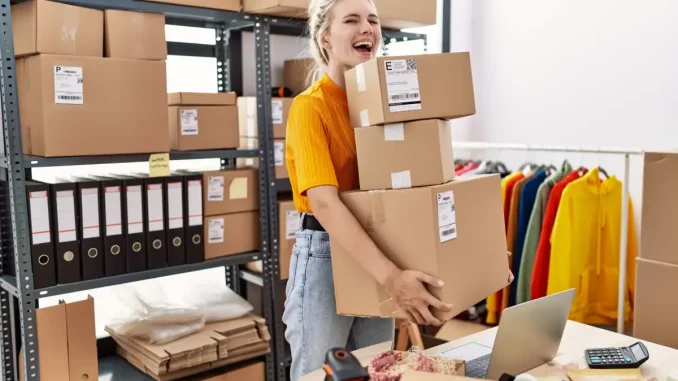 Eine Frau steht in ihrem Lager und hat ihre Ware im Online-Shop verkauft. Nun hält sie die fertigen Pakete zum Versenden in der Hand.