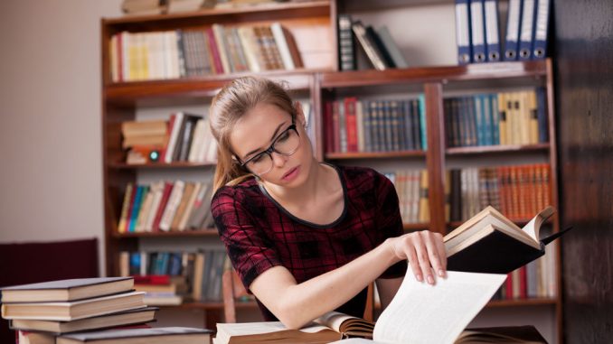 Junge Frau sitzt am Schreibtisch und lernt aufmerksam in einem Buch.