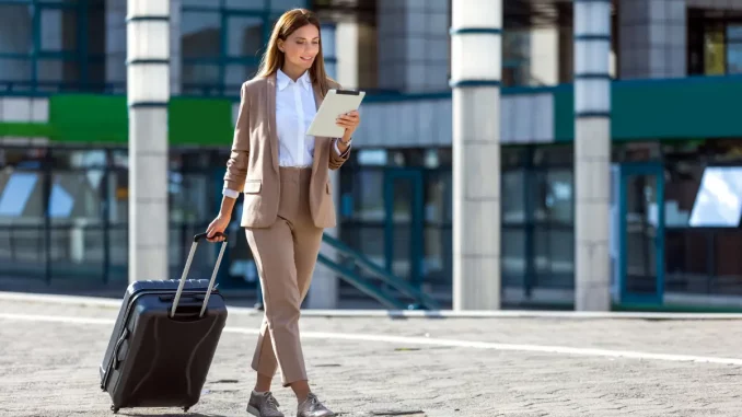 Eine Frau im Business-Outfit zieht während Geschäftsreise einen Koffer hinter sich her.