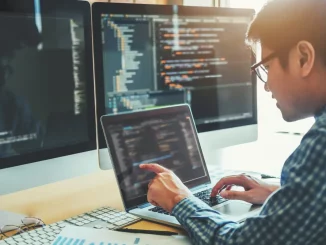 Ein Mann sitzt konzentriert an einem Schreibtisch vor einem Computerbildschirm, auf dem leicht verschwommene Codes zu sehen sind. Dieses Bild illustriert einen Artikel über IT-Karrieren, indem es den Fokus auf die tägliche Arbeit eines Programmierers legt.