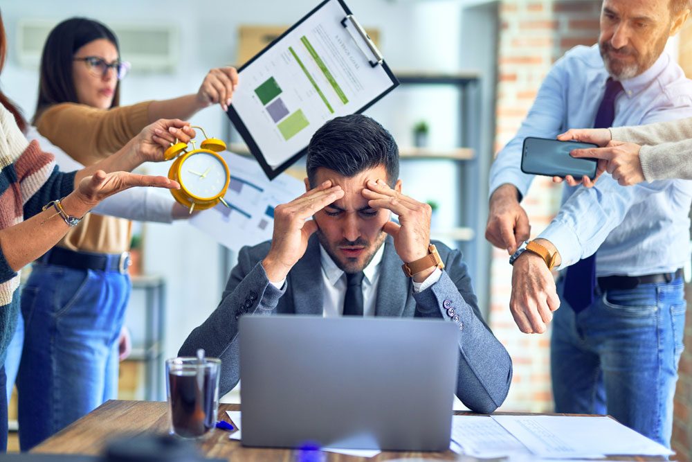 Mann fühlt sich am Arbeitsplatz von Kollegen gestresst Arbeitsstressbewältigung