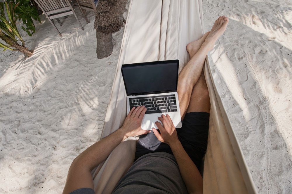 Mann liegt in der Hängematte und arbeitet am Laptop Workation Vorteile Arbeitnehmer