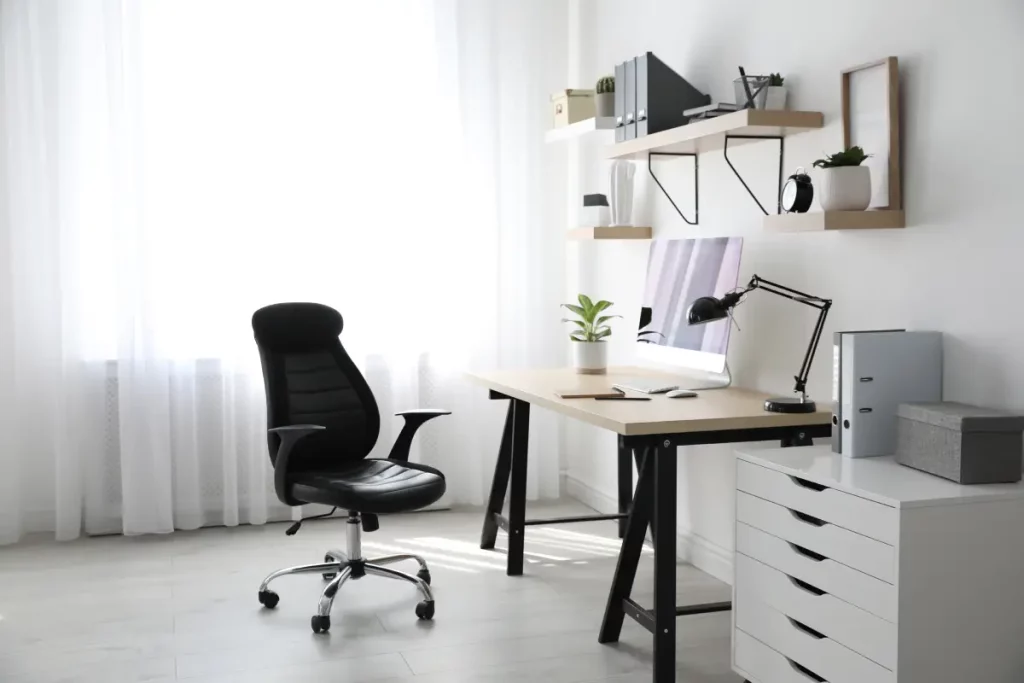 Ein kleines Büro mit Schreibtisch, Lampe, Schrank und Wandregalen