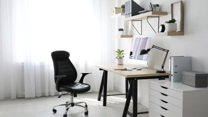 Ein kleines Büro mit Schreibtisch, Lampe, Schrank und Wandregalen