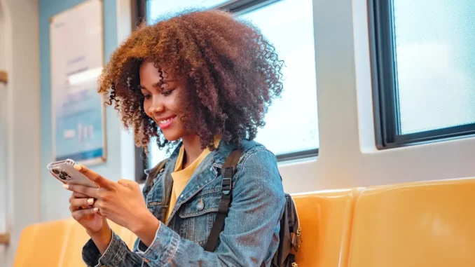 Junge Frau sitzt in der Bahn und schaut auf ihr Smartphone